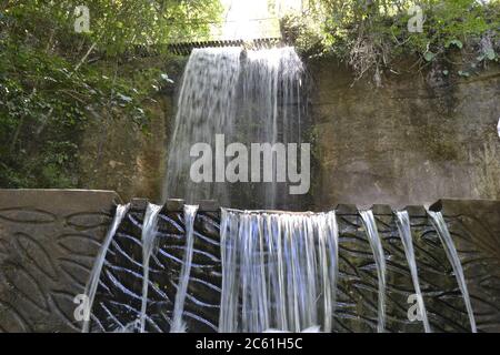 Wasserfall. Wasserfall aus Beton mit fallendem Wasser, Vegetation und Bäumen in einer Ansicht von unten nach oben, mit Motiven von Fischen im Beton Stockfoto