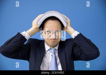 Überarbeiteter überholter Büroangestellter bedeckte seinen Kopf mit einem Stapel von Dokumenten Stockfoto