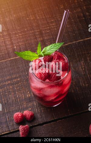 Frisches, eiskalter Beerensaft Getränk mit Minze, Sommer Himbeer Limonade im Glas mit Strohhalmen auf braunem Holzhintergrund, Winkelansicht selektiver Fokus Stockfoto