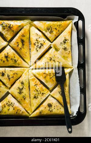 indische Samosa aus Phyllo mit würzigen Kartoffeln und Gemüse auf einem Backblech, fertig zum Backen im Ofen mit schwarzen Sesamsamen Stockfoto