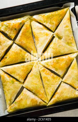 indische Samosa aus Phyllo mit würzigen Kartoffeln und Gemüse auf einem Backblech, fertig zum Backen im Ofen mit schwarzen Sesamsamen Stockfoto