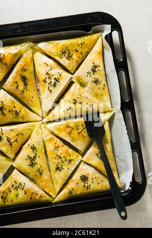 indische Samosa aus Phyllo mit würzigen Kartoffeln und Gemüse auf einem Backblech, fertig zum Backen im Ofen mit schwarzen Sesamsamen Stockfoto