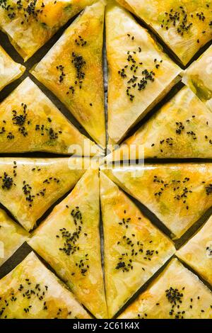 indische Samosa aus Phyllo mit würzigen Kartoffeln und Gemüse auf einem Backblech, fertig zum Backen im Ofen mit schwarzen Sesamsamen Stockfoto