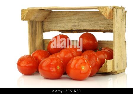 Ein Bündel frischer und farbenfroher italienischer Pflaumentomaten in einer Holzkiste auf weißem Hintergrund Stockfoto