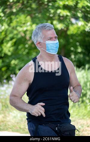 Ein Mann mittleren Alters läuft in Little Bay Park, während er eine chirurgische Maske trägt. In Whitestone, Queens, New York City. Stockfoto