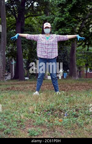 Eine asiatisch-amerikanische Frau macht Tai Chi Übungen, während sie eine Maske und Gummihandschuhe trägt. Im Kissena Park in Flushing, Queens, New York City. Stockfoto