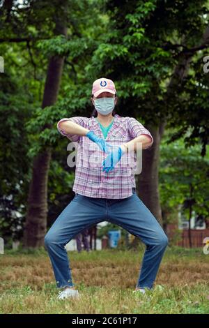 Eine asiatisch-amerikanische Frau macht Tai Chi Übungen, während sie eine Maske und Gummihandschuhe trägt. Im Kissena Park in Flushing, Queens, New York City. Stockfoto