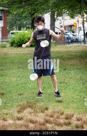 Ein asiatischer amerikanischer Mann mit einer chirurgischen Maske führt auf einem chinesischen Jojo namens Diablo auf. In Kissena Park, Flushing, New York City. Stockfoto