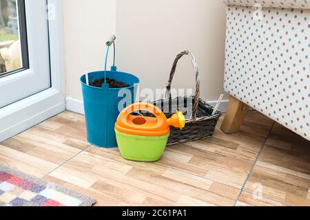 Ein Kind ist hell gefärbt, orange grün, Gießkanne durch einen blauen Eimer und Korb voller Kompost und Samen. Stockfoto