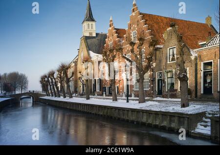 Malerischer Winterblick auf eine Reihe historischer Häuser und Kirche mit einer kleinen Brücke im malerischen Dorf Sloten in den Niederlanden Stockfoto