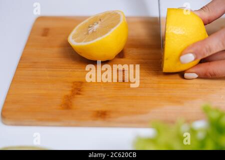 Nahaufnahme der Hand einer Frau, die mit einem Küchenmesser an Bord frische Zitrone schneidet. Stockfoto