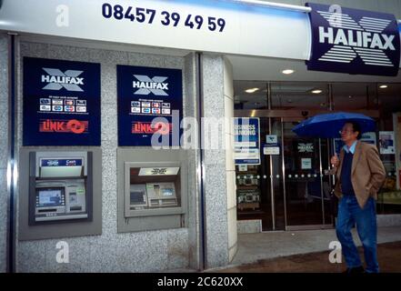 Sutton Surrey England Mann hält Regenschirm Gehen durch Halifax Geldautomaten im Regen Stockfoto