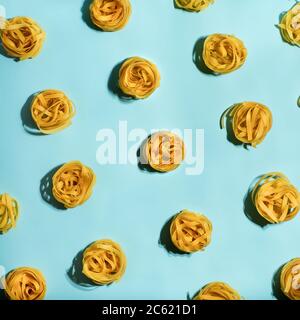Pasta Art. Tagliatelle auf blauem pastellfarbenem Hintergrund in hartem Licht. Kreatives Layout mit Nudelnudeln, Draufsicht oder Flat Lay. Quadratisches Erntegut. Kreatives Design für Menü der italienischen Küche mit Kopierraum Stockfoto