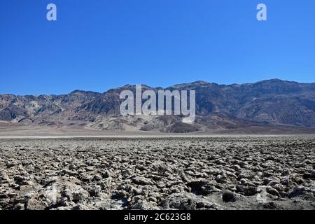 Devils Golfplatz im Death Valley Nationalpark. Scharfe und zerklüftete Salzkristalle steigen an einem klaren Tag mit Bergen im Hintergrund aus dem Boden. Stockfoto