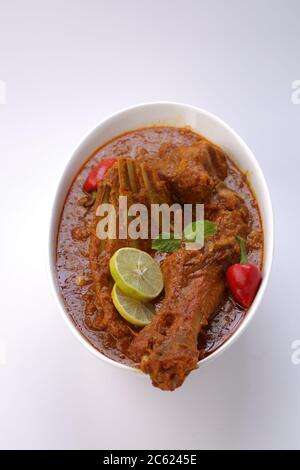 Draufsicht auf Mutton Curry oder Lamm Curry, würziges und leckeres Gericht garniert mit Minzblatt, Zitronenscheiben und rotem Chili in einer weißen ovalen Schüssel mit weiß Stockfoto