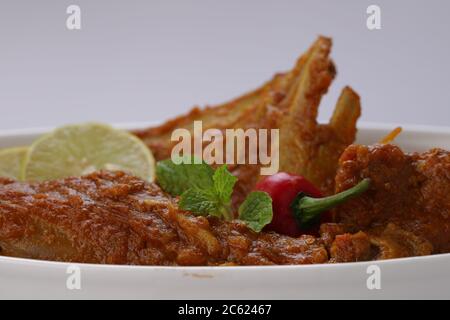 Nahaufnahme von Mutton Curry oder Lamm Curry, würzige und köstliche Gericht garniert mit Minzblatt, Zitronenscheiben und rote Chili in einer weißen ovalen Schüssel mit weiß Stockfoto
