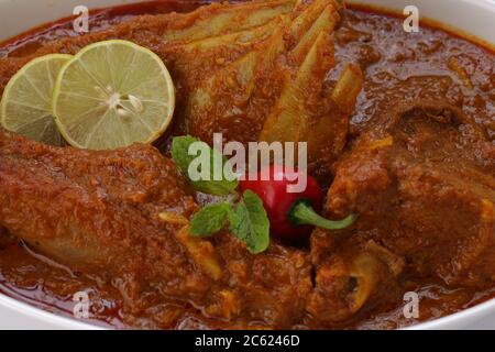Nahaufnahme von Mutton Curry oder Lamm Curry, würzige und köstliche Gericht garniert mit Minzblatt, Zitronenscheiben und rote Chili in einer weißen ovalen Schüssel mit weiß Stockfoto