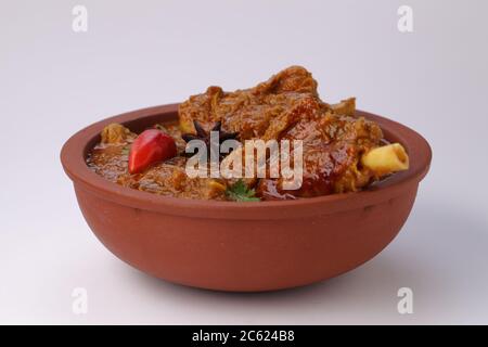 Hammelcurry oder Lammcurry, würziges und köstliches Gericht garniert mit Korianderblatt, roter Chili und Sternanis in einer Steingutschüssel mit Weiß Stockfoto