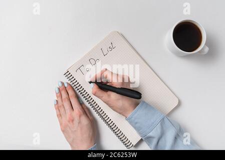Um Listentext im Copybook zu tun. Weibliche Hände schreiben im Notizbuch. Notizblock und Tasse Kaffee auf weißem Hintergrund Stockfoto