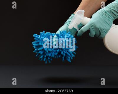 Hände in Nitrilhandschuhe mit einer Plastikflasche mit Waschflüssigkeit und einem Lappen auf dem schwarzen Hintergrund. Wasch- und Reinigungsset. Stockfoto