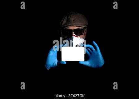 Ein älterer Mann in einem Atemschutzgerät und Handschuhen zum Schutz gegen Covid-19 hält eine weiße Leerstelle für Text Stockfoto