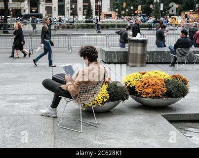 Erwachsene männlich gesehen sitzen und mit einer Marke von Computer-Tablet neben dem Flaggschiff Einzelhandel Computer, Telefon und Tablet-Hersteller in der Nähe von Central Park, NYC. Stockfoto