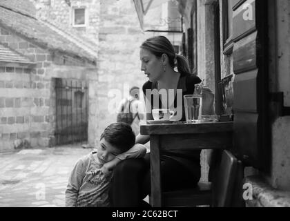 Montenegro, 22. September 2019: Verschlafener Junge und seine Mutter verbringen Zeit in einem Straßencafé in der Altstadt von Kotor (s/W) Stockfoto