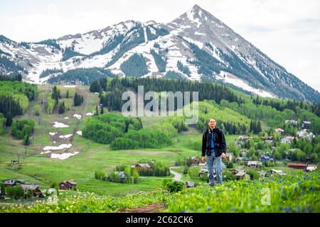 Mann steht weit entfernt Wandern auf dem Snodgrass Trail mit Blick auf Mount Crested Butte, Colorado Peak und Ski Dorf Stadtbild im Sommer Stockfoto