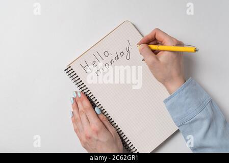 Hallo montag Text im Copybook. Weibliche Hände schreiben Notiz in Notepad. Weißer Hintergrund. Stockfoto