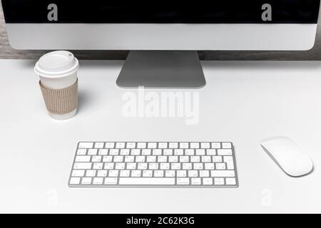 Arbeitsbereich und leerer Bildschirm-Desktop-Computer. Morgenkaffee, Uhren, Accessoires auf einem weißen Tisch. Stockfoto