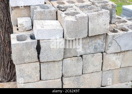 Stapel von gebrauchten und beschädigten grauen Zunder Blöcke in der Nähe des Baumes. Konzept der Konstruktionsidee Stockfoto