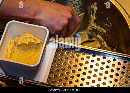 Der Knöpfler in Aktion. Kässpätzler werden auch Käsknöpfle genannt. Frische Pasta mit Reibe - typisch österreichische Käsepasta - Teig fällt in kochendes Wasser Stockfoto