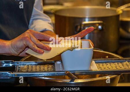 Der Knöpfler in Aktion. Kässpätzler werden auch Käsknöpfle genannt. Frische Pasta mit Reibe - typisch österreichische Käsepasta - Teig fällt in kochendes Wasser Stockfoto