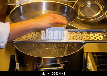 Der Knöpfler in Aktion. Kässpätzler werden auch Käsknöpfle genannt. Frische Pasta mit Reibe - typisch österreichische Käsepasta - Teig fällt in kochendes Wasser Stockfoto