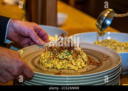 Der Knöpfler in Aktion. Kässpätzler werden auch Käsknöpfle genannt. Frische Pasta mit Reibe - typisch österreichische Käsepasta - Teig fällt in kochendes Wasser Stockfoto