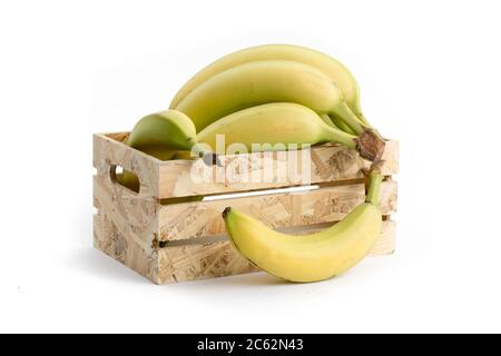 Natürlich aussehende reife gelbe Bananen in einer Holzkiste und Einer fällt isoliert auf Weiß aus Stockfoto
