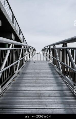 Einsame Frau sah an einem Tisch oben auf diesem Metallsteg sitzen, der sich an einem Hafen befindet. Stockfoto