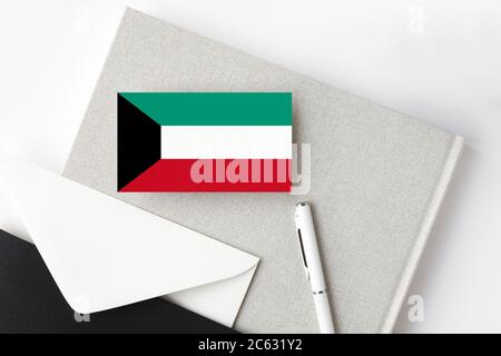 Kuwait-Flagge auf minimalistischen Buchstaben Hintergrund. Nationaler Einladungsumschlag mit weißem Stift und Notizbuch. Kommunikationskonzept. Stockfoto