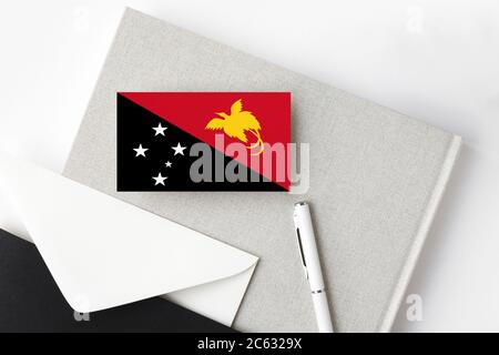 Papua-Neuguinea-Flagge auf minimalistischem Buchstabenhintergrund. Nationaler Einladungsumschlag mit weißem Stift und Notizbuch. Kommunikationskonzept. Stockfoto