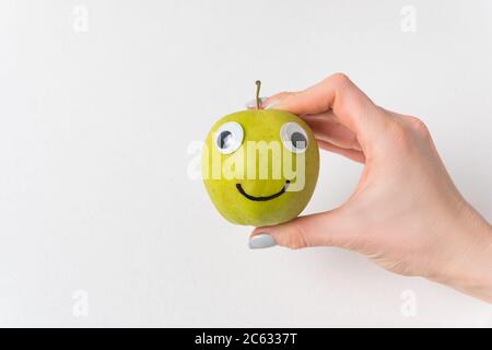 Weibliche Hand hält kleinen Apfel Lächeln mit Googly Augen. Weißer Hintergrund. Diät und Gewichtsverlust Konzept. Stockfoto