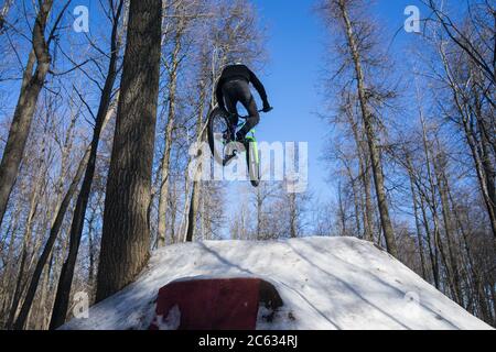 Guy springt auf einem Sprungbrett auf einem Fahrrad im Winter. Winter Dirt Jumping Stockfoto