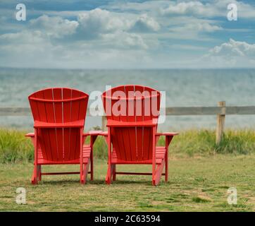Zwei rote Adirondack-Stühle mit Blick auf das Meer im PEI-Nationalpark, Prince Edward Island. Stockfoto