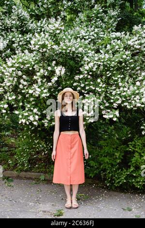 Junge Frau in einem Sommerhut geht unter der Blüte Bäume Stockfoto