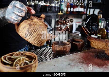 Ein männlicher Barkeeper gießt Tee aus einer Tonteapot in eine Keramikschale. Prozess Brühtee, Tee Zeremonie Stockfoto