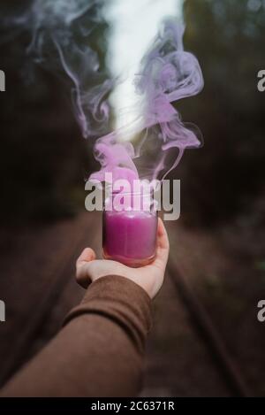Blauer Rauch aus einer Tasse, die von einem Mann gehalten wird Hand auf einem Wald Stockfoto