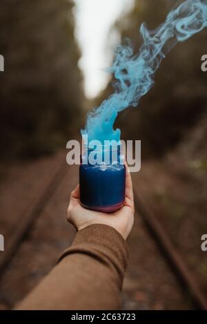 Blauer Rauch aus einer Tasse, die von einem Mann gehalten wird Hand auf einem Wald Stockfoto