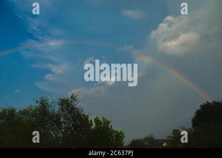 Regenbogen über Bäumen und blauer Himmel mit Wolken Stockfoto