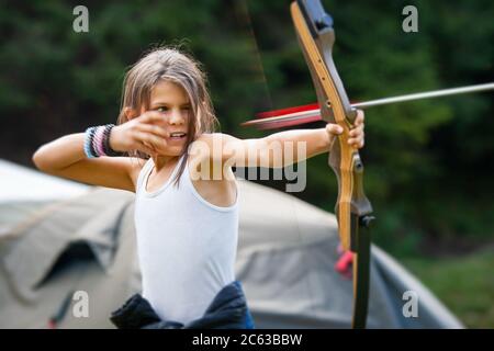 PADIS, KREIS BIHOR, RUMÄNIEN - AUGUST.25.2016: Glückliches Mädchen schießen mit Pfeil und Bogen in einem Waldlager mit Zigeunerkindern Stockfoto