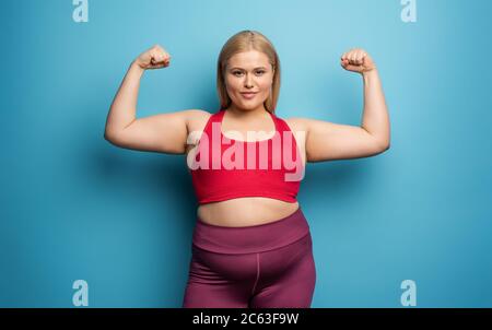 Fat Girl macht zu Hause Fitness-Studio. Zufriedener Ausdruck. Hintergrund Zyan Stockfoto