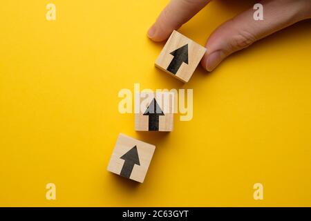 Das Konzept der Entwicklung und des Erfolgs im Geschäft. Holzwürfel mit Pfeil auf gelbem Hintergrund Stockfoto